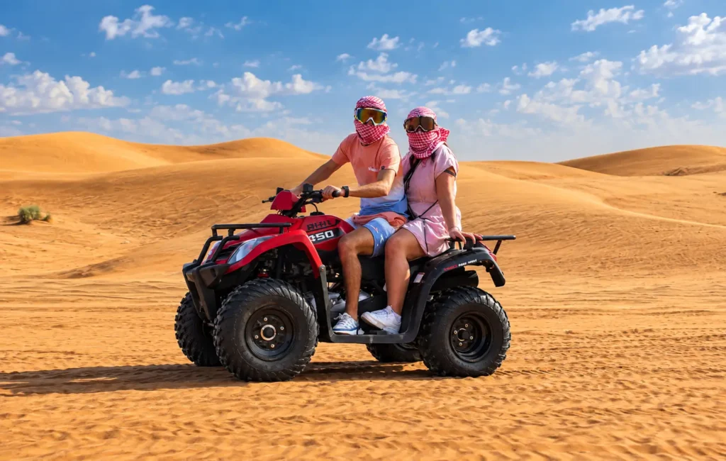 Two riders on a double-seater quad bike exploring open desert dunes during quad biking Dubai.