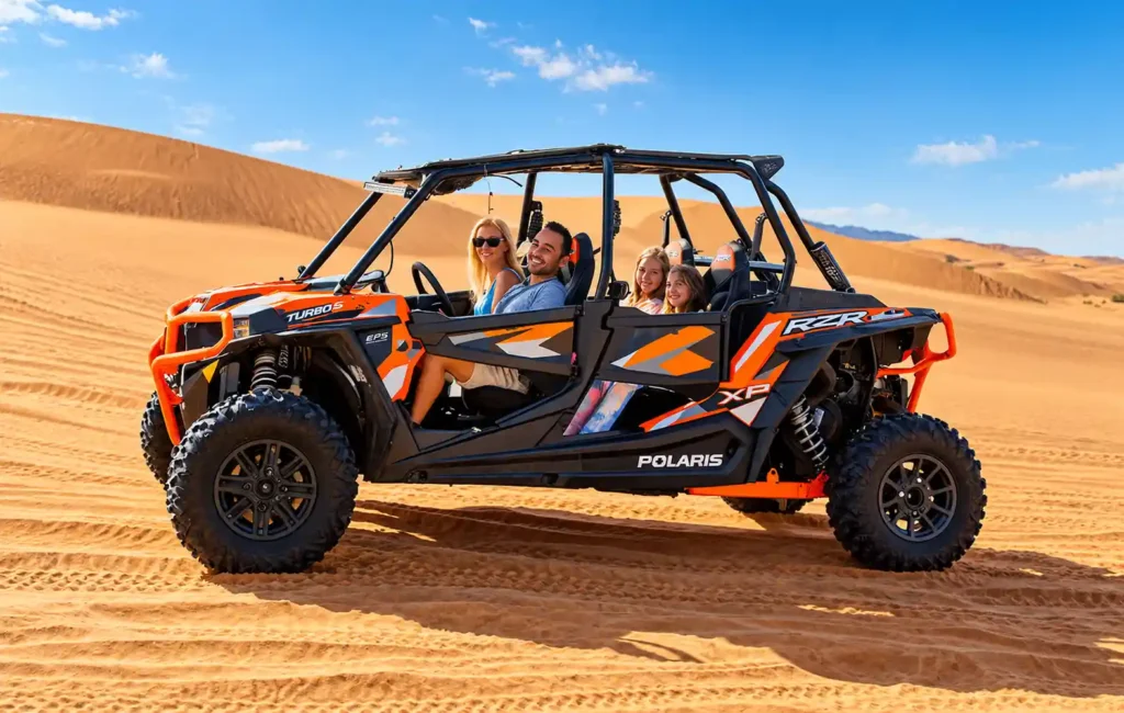 Four people riding in a 4-seater Polaris RZR dune buggy across the Dubai desert dunes.