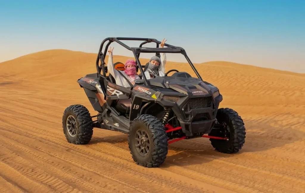 Two riders wearing safety helmets inside a 2-seater Polaris RZR dune buggy in Dubai.