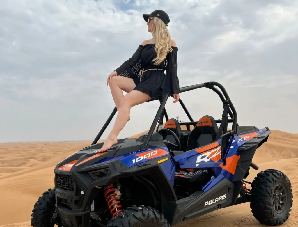 A rider driving an orange Polaris RZR dune buggy across the desert dunes during a Dune Buggy Dubai tour.