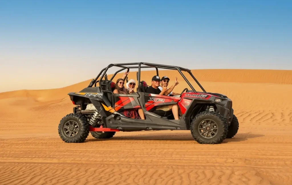 alt: Four passengers wearing safety gear inside a 4-seater Polaris dune buggy in Dubai desert.