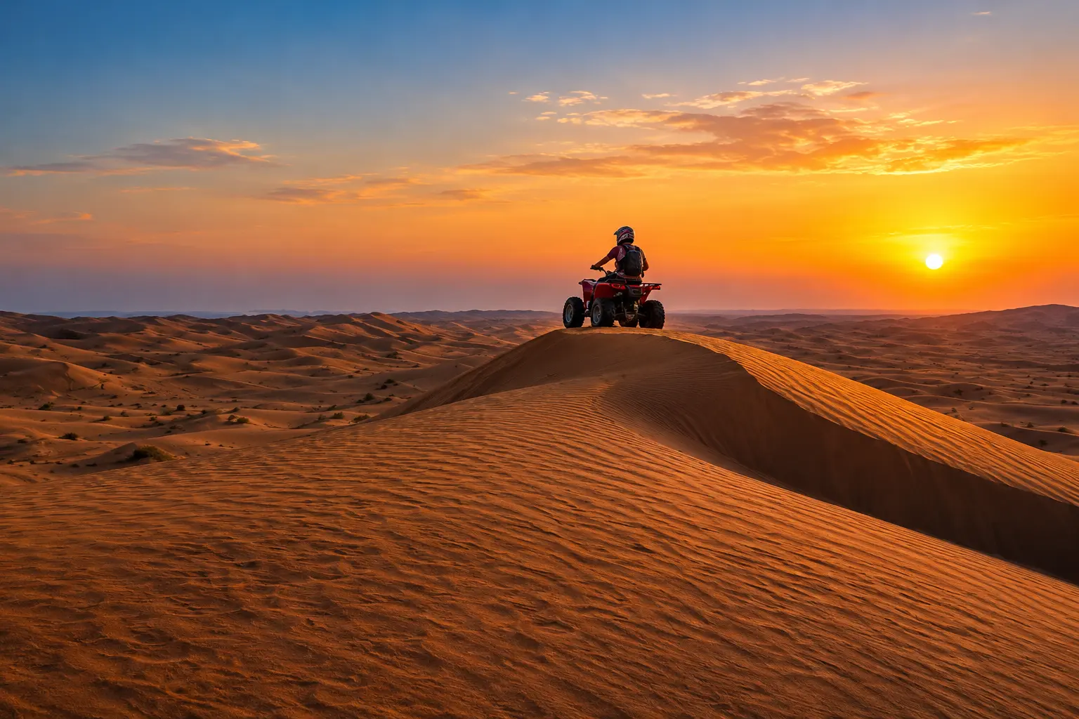 A person riding a red quad bike atop a sand dune during a vibrant golden desert sunrise.