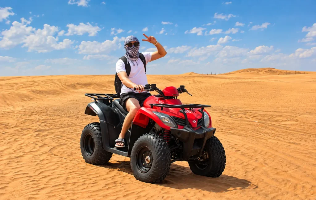 Woman riding a red ATV during a quad biking Dubai adventure across desert dunes.