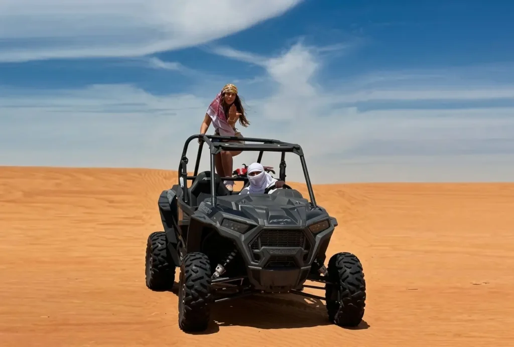 Two passengers riding in a 2-seater Polaris dune buggy across the Dubai desert.