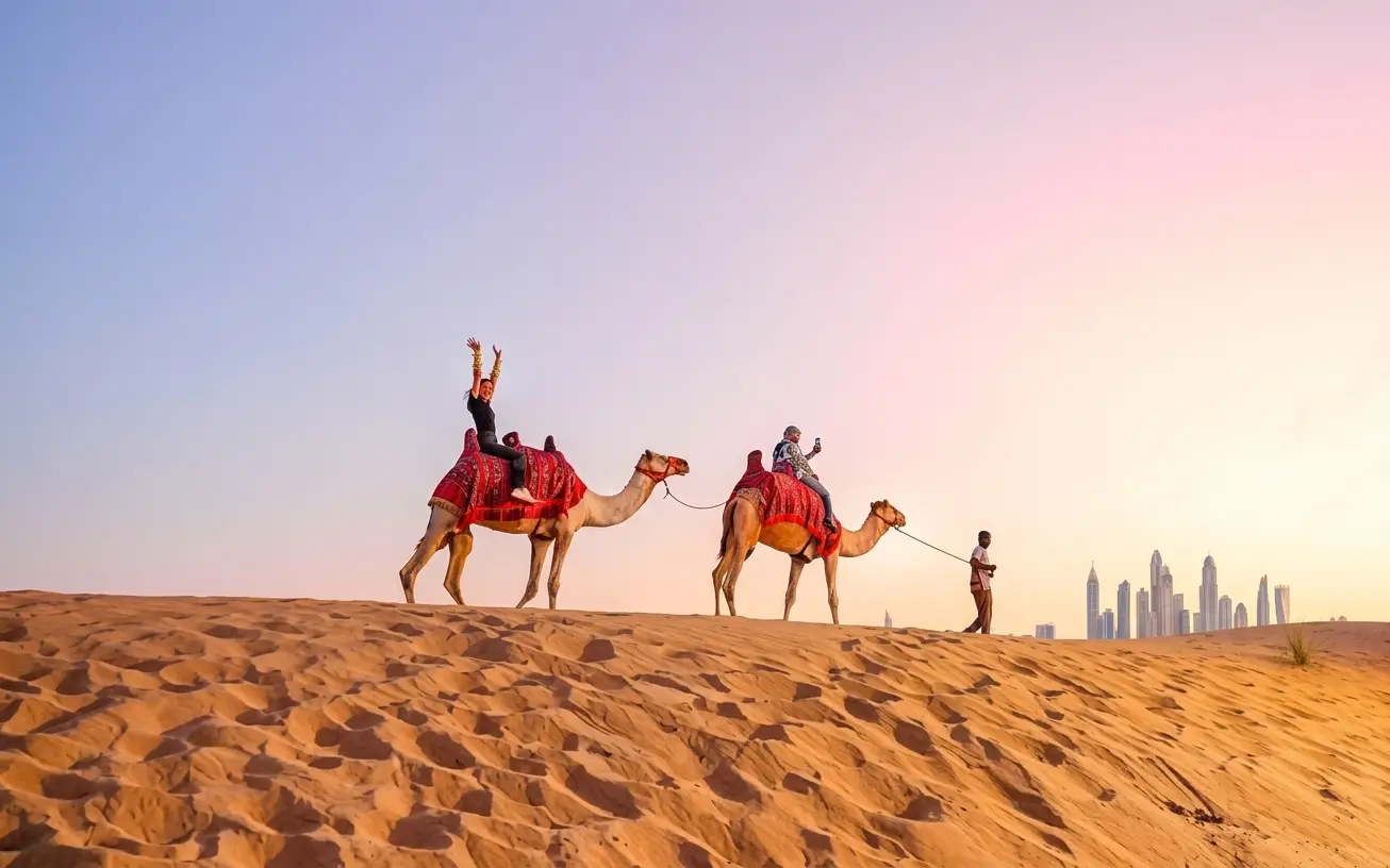 Tourists riding camels across the golden desert sand dunes during a safari in Dubai