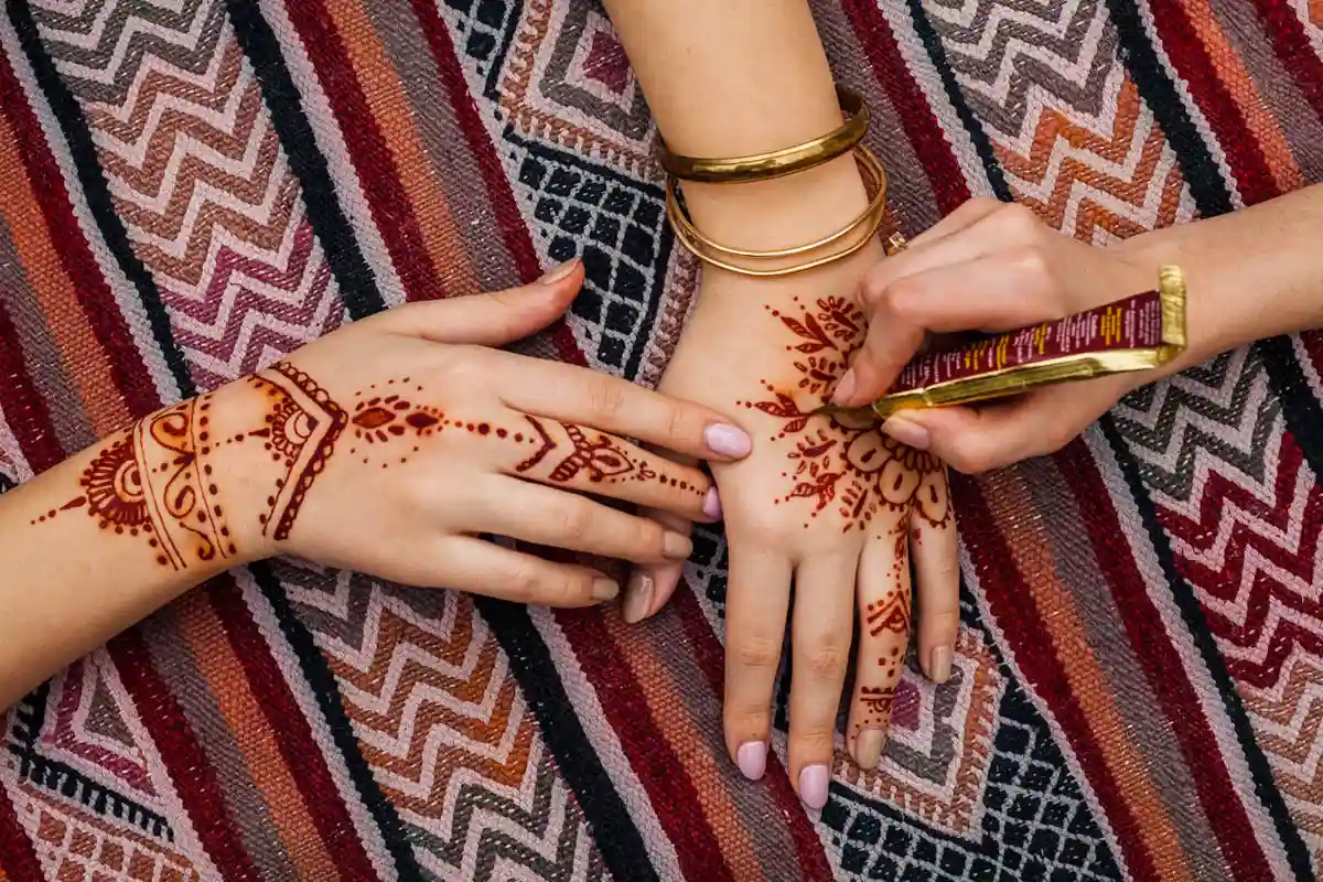 alt: Artist applying intricate traditional henna tattoo design on a woman's hand in Dubai.
