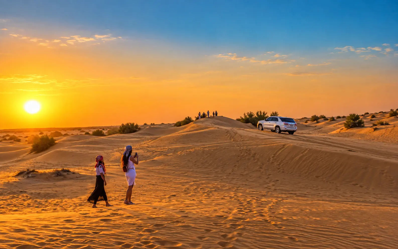 Two women taking photos on golden desert dunes at sunrise with a 4x4 SUV.