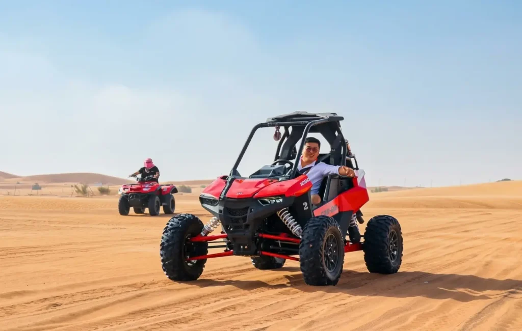 Single-seat Polaris RZR dune buggy driving across red desert sand dunes in Dubai.