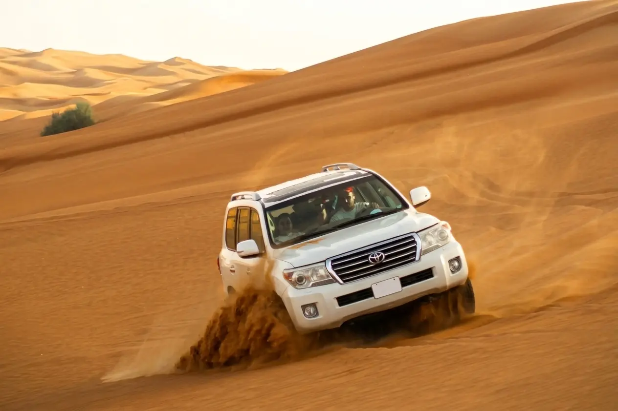 White 4x4 Land Cruiser speeding across golden sand dunes during a desert safari in Dubai
