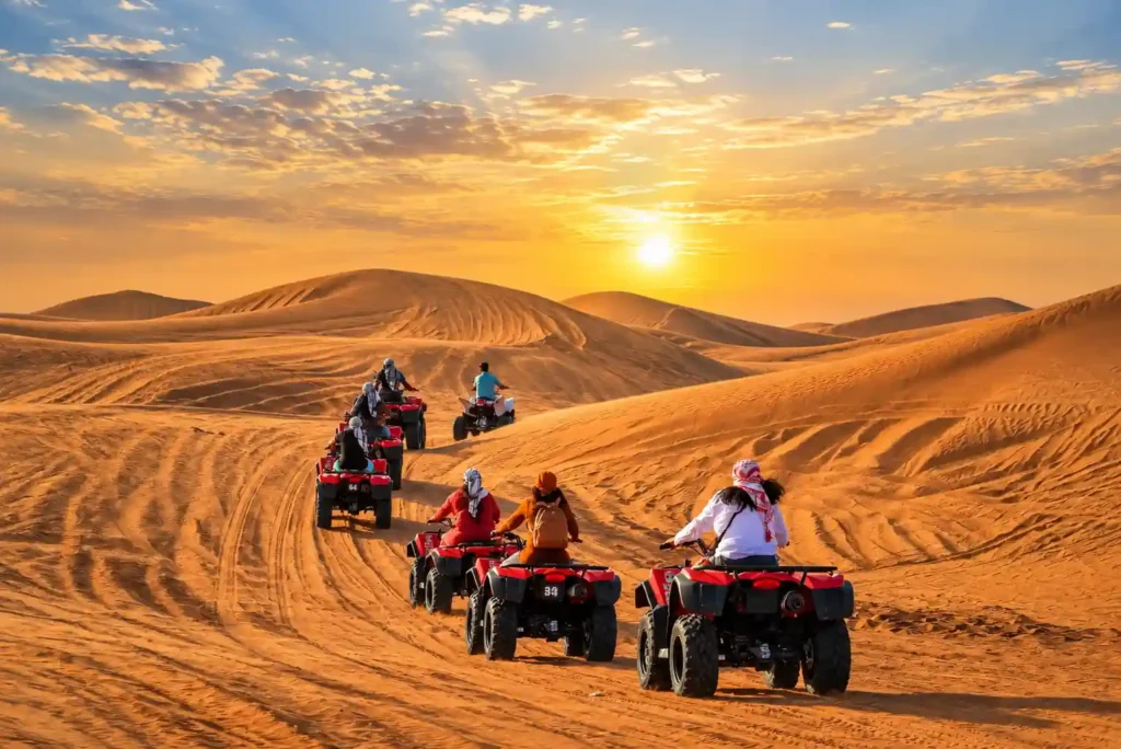 Tourists riding quad bikes self-drive across the red sand dunes during a desert safari Dubai adventure.