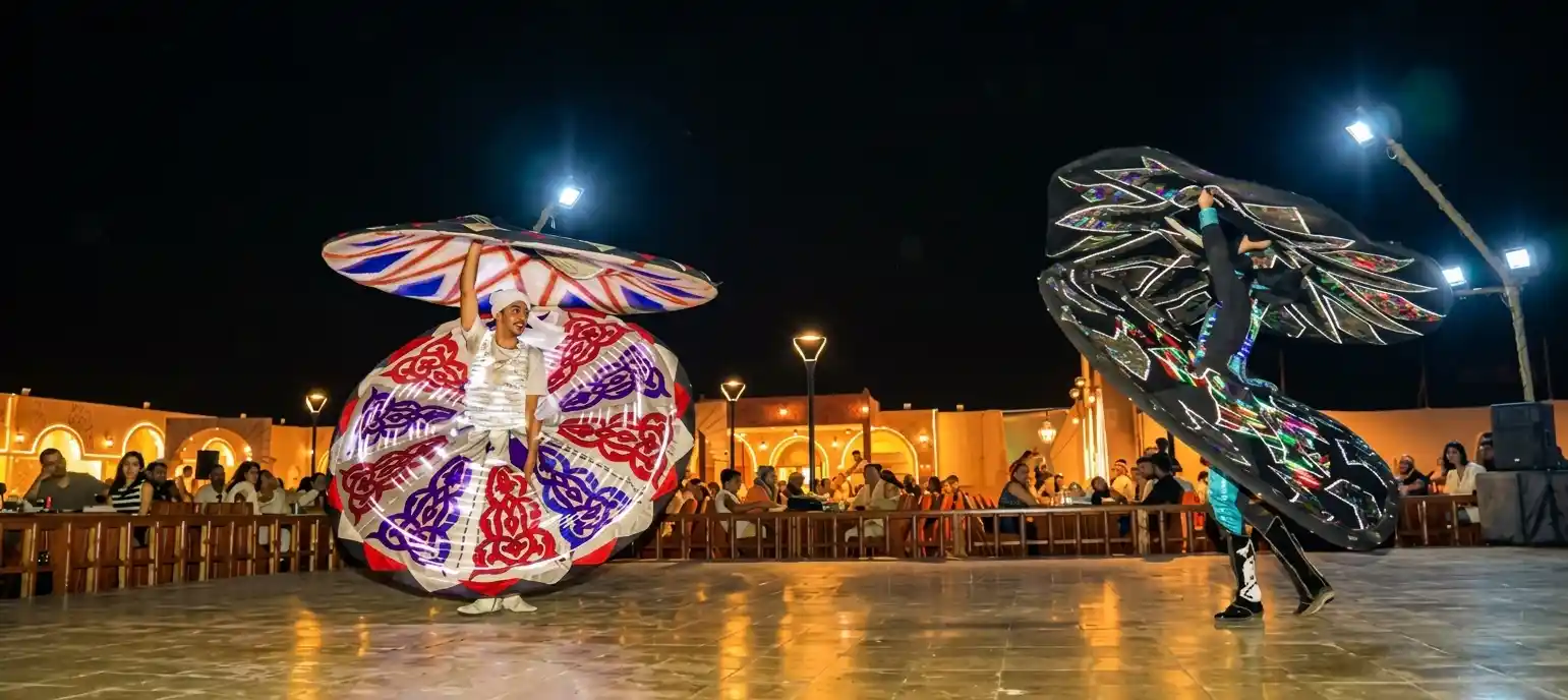 Male performer spinning in a colorful illuminated Tanoura costume at a Dubai desert camp show